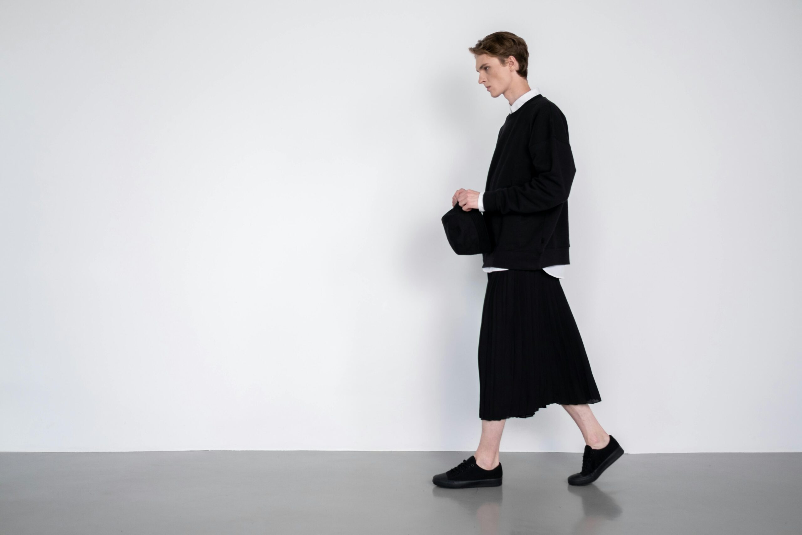 A minimalist black waterproof poncho model walking under an umbrella